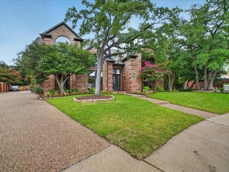 5201 Windjammer Road, Plano, TX 75093 Brick facade residence featuring an arched window, mature trees, and a textured driveway