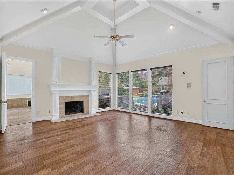 5201 Windjammer Road, Plano, TX 75093 Living area featuring a vaulted ceiling with exposed beams, wood-finish flooring, a fireplace with a stone surround and white mantle, and large windows overlooking an outdoor pool