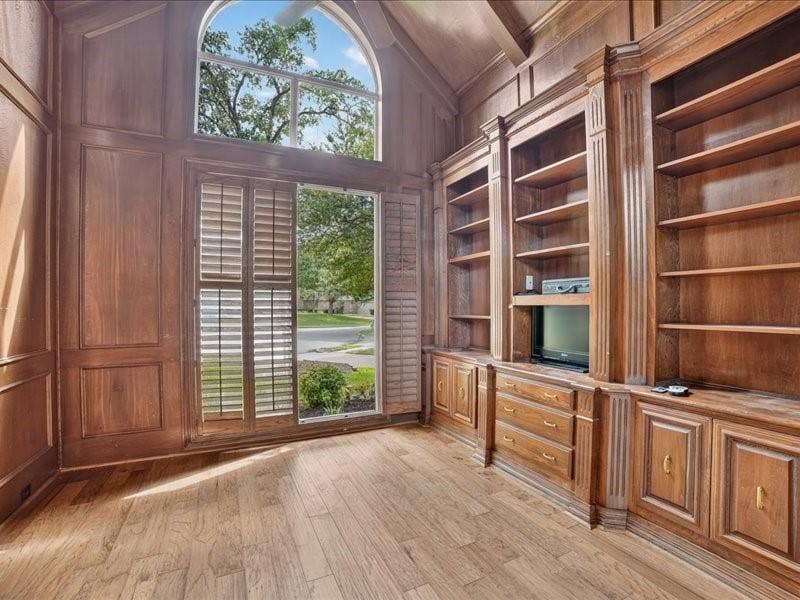 5201 Windjammer Road, Plano, TX 75093 Room featuring extensive wood paneling, built-in shelving, wood-finish flooring, and an arched window with plantation shutters