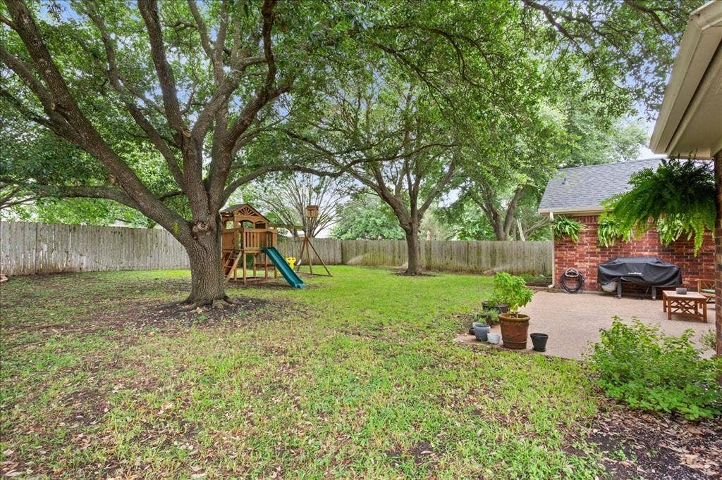 10308 Eagle Mountain Drive, Waco, TX 76712 Expansive backyard featuring mature trees, a wooden privacy fence, a brick exterior with a dark shingle roof, and a concrete patio