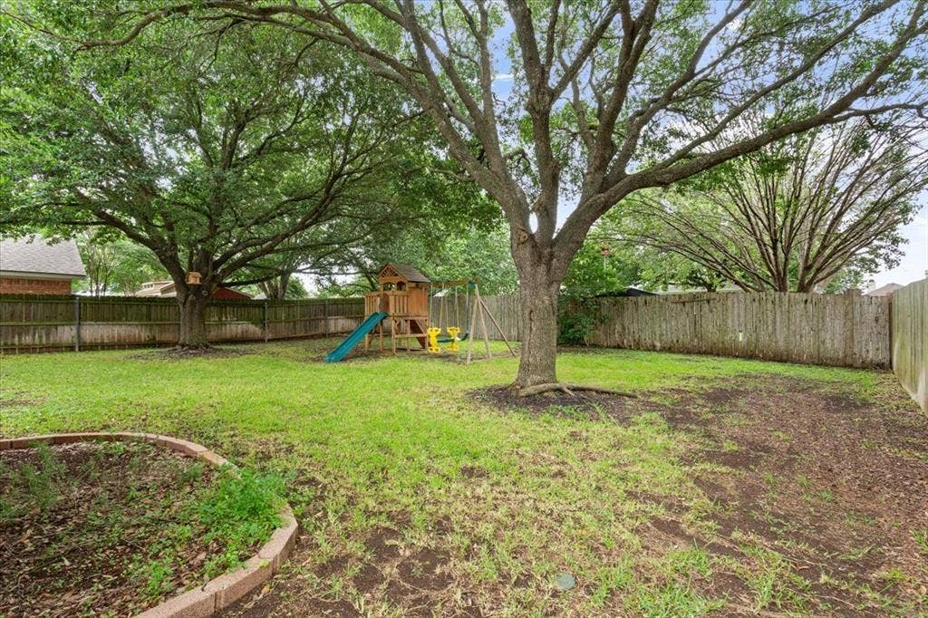 10308 Eagle Mountain Drive, Waco, TX 76712 Expansive backyard featuring mature trees, a wooden privacy fence, and a defined garden bed with brick edging