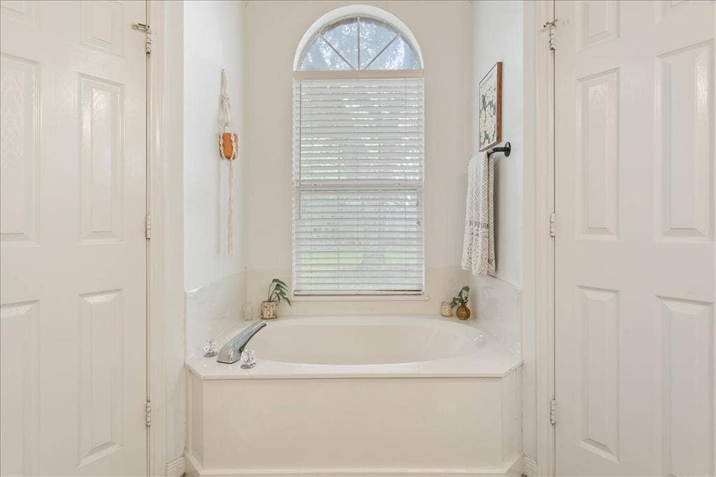 10308 Eagle Mountain Drive, Waco, TX 76712 Soaking tub with chrome fixtures, arched window with horizontal blinds, and white paneled doors