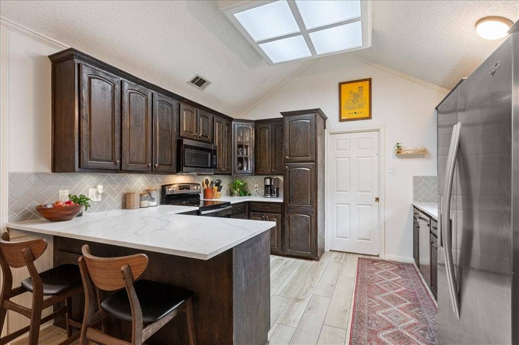 10308 Eagle Mountain Drive, Waco, TX 76712 Kitchen featuring dark wood cabinetry, light countertops, and a white subway tile backsplash in a herringbone pattern