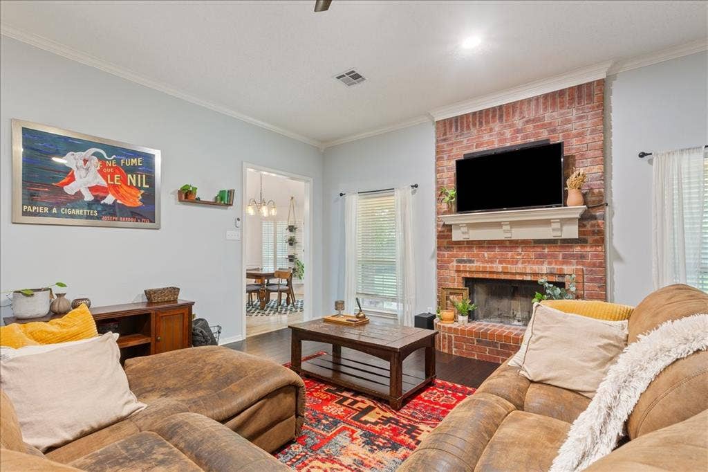 10308 Eagle Mountain Drive, Waco, TX 76712 Living area featuring a brick fireplace with a white mantel, dark wood-finish flooring, light-colored walls, crown molding, and a visible doorway to an adjacent room