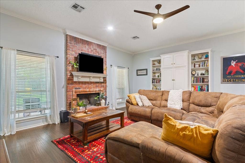 10308 Eagle Mountain Drive, Waco, TX 76712 Living area featuring a brick fireplace with a white mantel, wood-finish flooring, built-in shelving, and crown molding