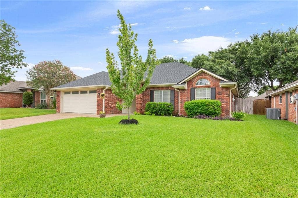 10308 Eagle Mountain Drive, Waco, TX 76712 Traditional brick-front residence featuring a two-car garage with a panel door, a dark shingle roof, and a meticulously maintained front lawn