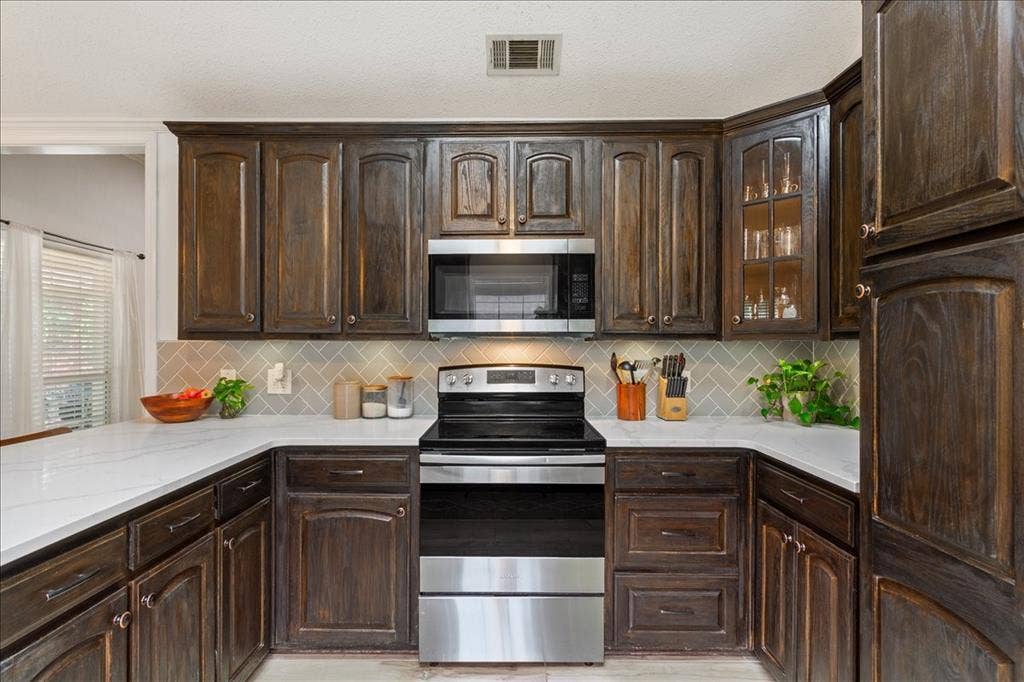 10308 Eagle Mountain Drive, Waco, TX 76712 U-shaped kitchen featuring dark wood cabinetry, light-toned countertops, a stainless steel range, and a subway tile backsplash in a herringbone pattern