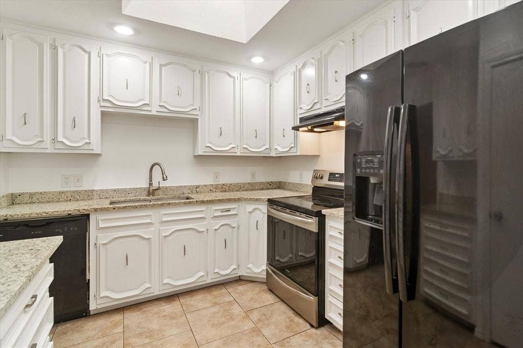 3318 Wells Drive, Plano, TX 75093 Kitchen featuring white cabinetry, light-toned granite countertops, stainless steel appliances, a black refrigerator, and tiled flooring