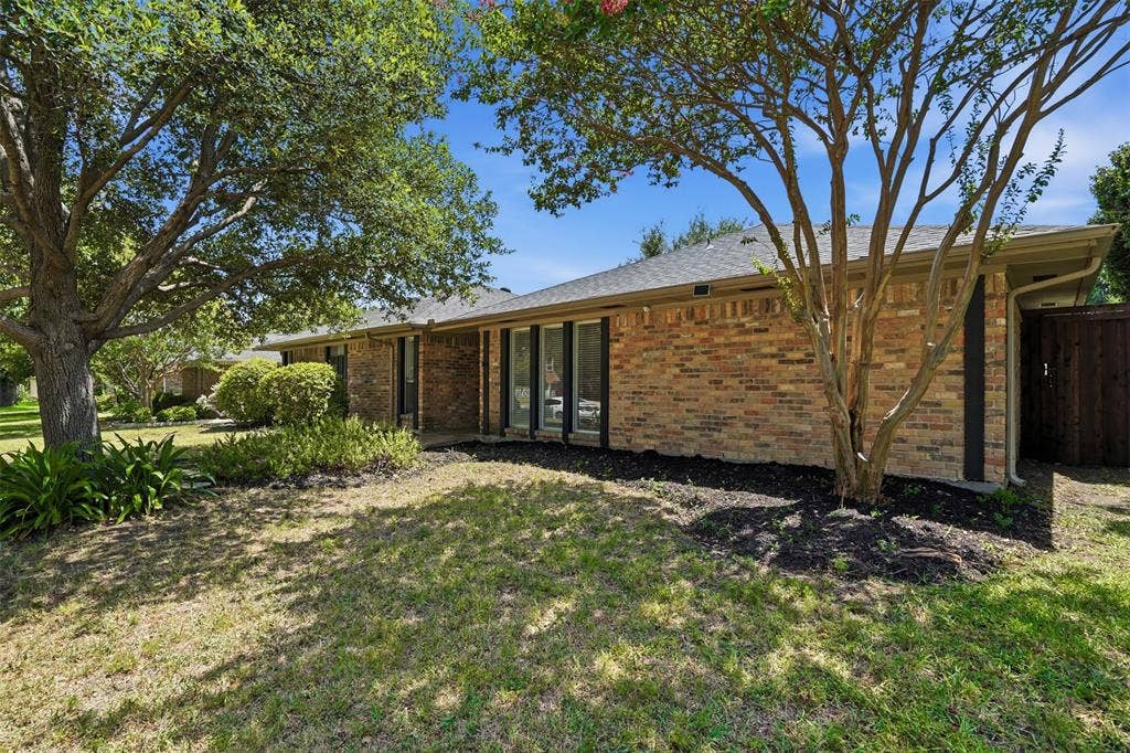 1000 Lexington Drive, Plano, TX 75075 Brick exterior featuring a dark asphalt shingle roof, black-framed windows, mature trees, and established landscaping