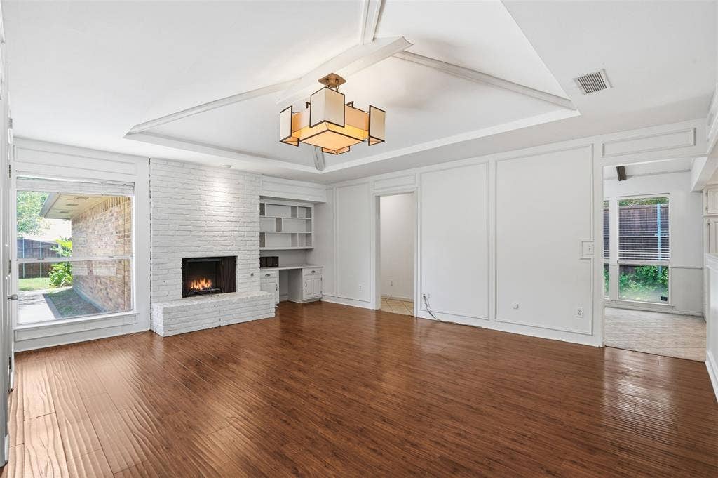 1000 Lexington Drive, Plano, TX 75075 Spacious living area featuring wood-finish flooring, a white brick fireplace, and extensive built-in shelving