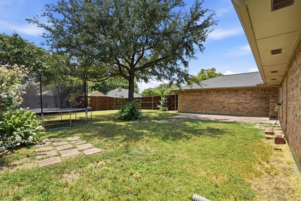 1000 Lexington Drive, Plano, TX 75075 Expansive rear yard featuring a large mature tree, a paved patio area, and a brick exterior wall