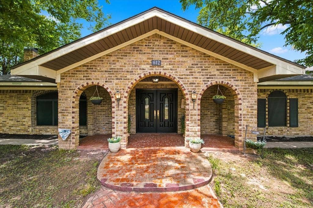612 W Highland Street, West, TX 76691 Brick facade residence featuring a covered entry with dual arches, double entry doors, brick paver walkway, and dark window shutters
