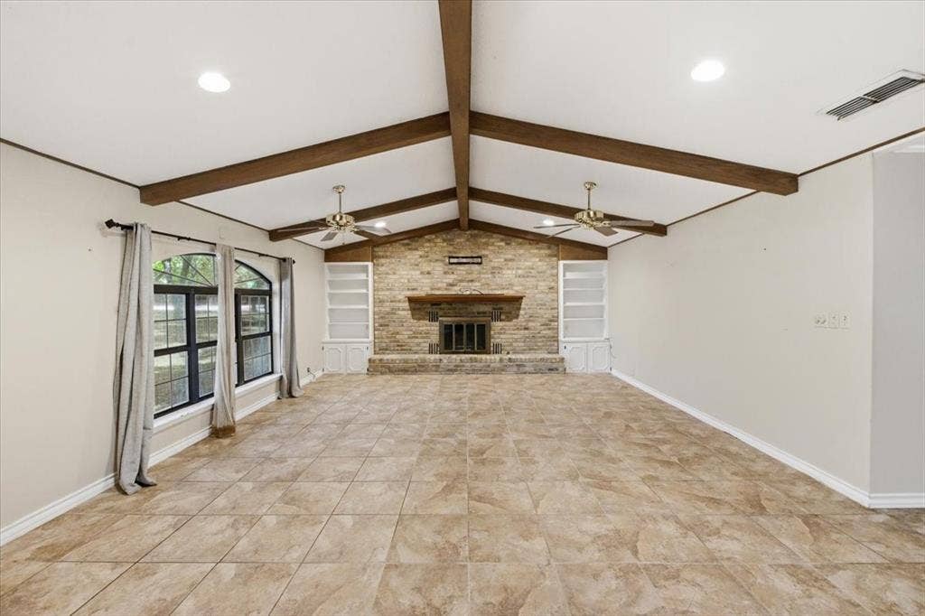 612 W Highland Street, West, TX 76691 Spacious room featuring tile floors, a vaulted ceiling with exposed wood beams, a brick fireplace, and built-in shelving