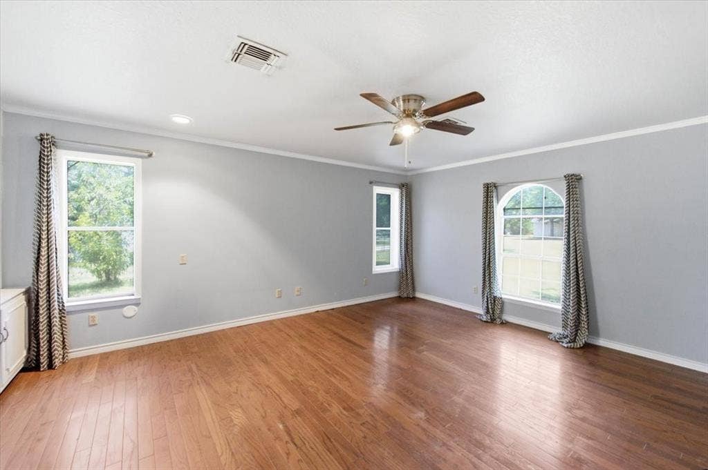 612 W Highland Street, West, TX 76691 Spacious primary bedroom featuring beautiful natural light, wood-finish flooring, light gray walls, and white crown molding