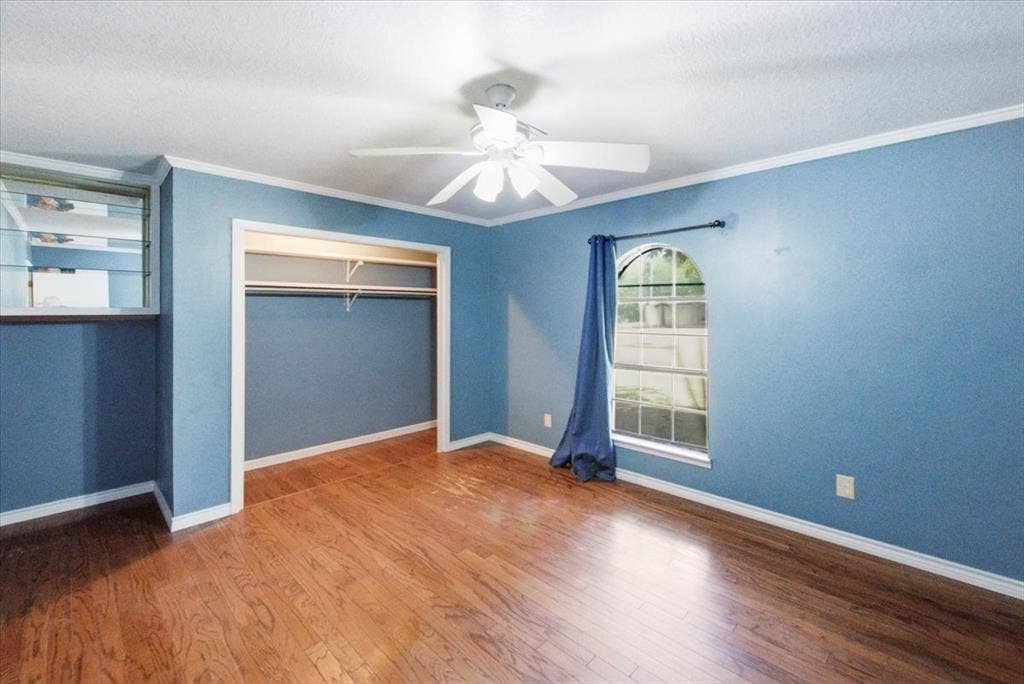 612 W Highland Street, West, TX 76691 Spacious secondary bedroom featuring wood-finish flooring, an arched window, crown molding, a ceiling fan, a built-in display shelf, and an open closet with shelving