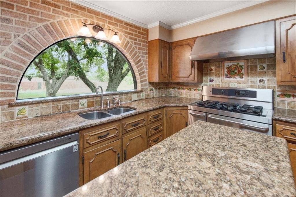 612 W Highland Street, West, TX 76691 Kitchen featuring a brick archway framing a semi-circular window, stainless steel appliances including a gas range, and ample counter space with a movable kitchen island