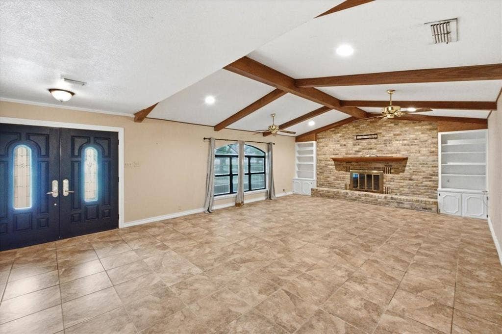 612 W Highland Street, West, TX 76691 Entryway into a spacious living room with brick woodburning fireplace featuring built-in bookshelves with a vaulted, beamed ceiling with two ceiling fans