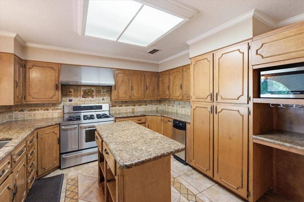 612 W Highland Street, West, TX 76691 Kitchen featuring wood-finish cabinetry, a large central island with a granite countertop, pantry with pull-out shelves for full access, stainless steel appliances, and tile flooring