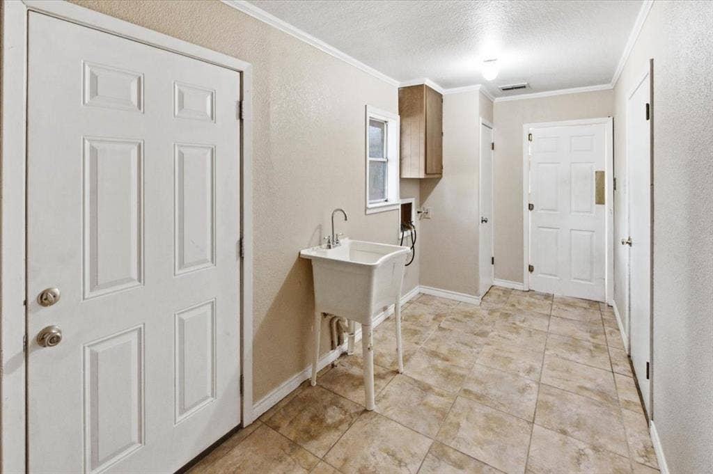 612 W Highland Street, West, TX 76691 Very spacious utility room featuring neutral-toned tile flooring, a utility sink, full sized washer & dryer connections, a swinging door for easy access carrying laundry, a tankless gas water heater (in the closet), access to the back patio and the garage, and a window providing natural light