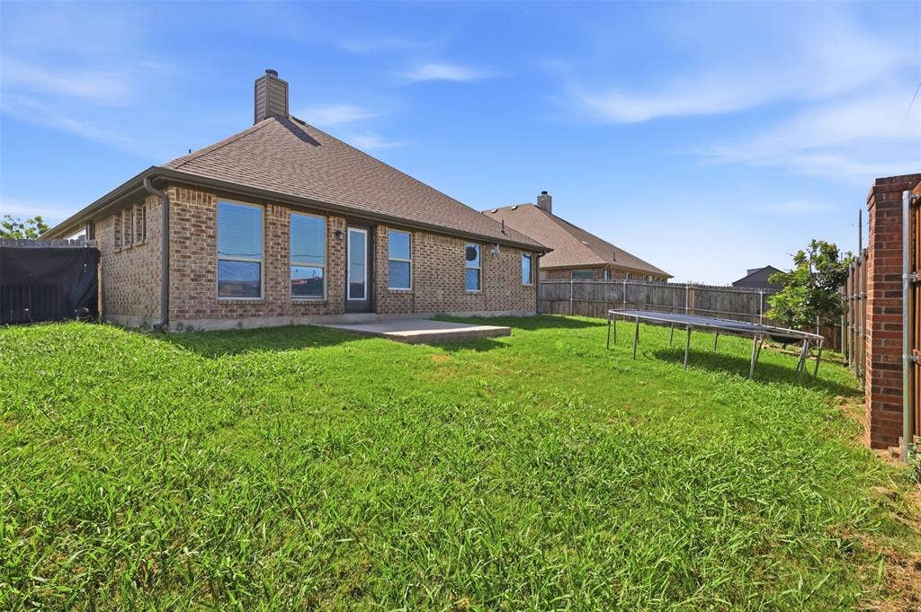 5003 Spruce Street, Krum, TX 76249 Expansive green space featuring a concrete patio, brick exterior, multiple large windows, and a fenced perimeter