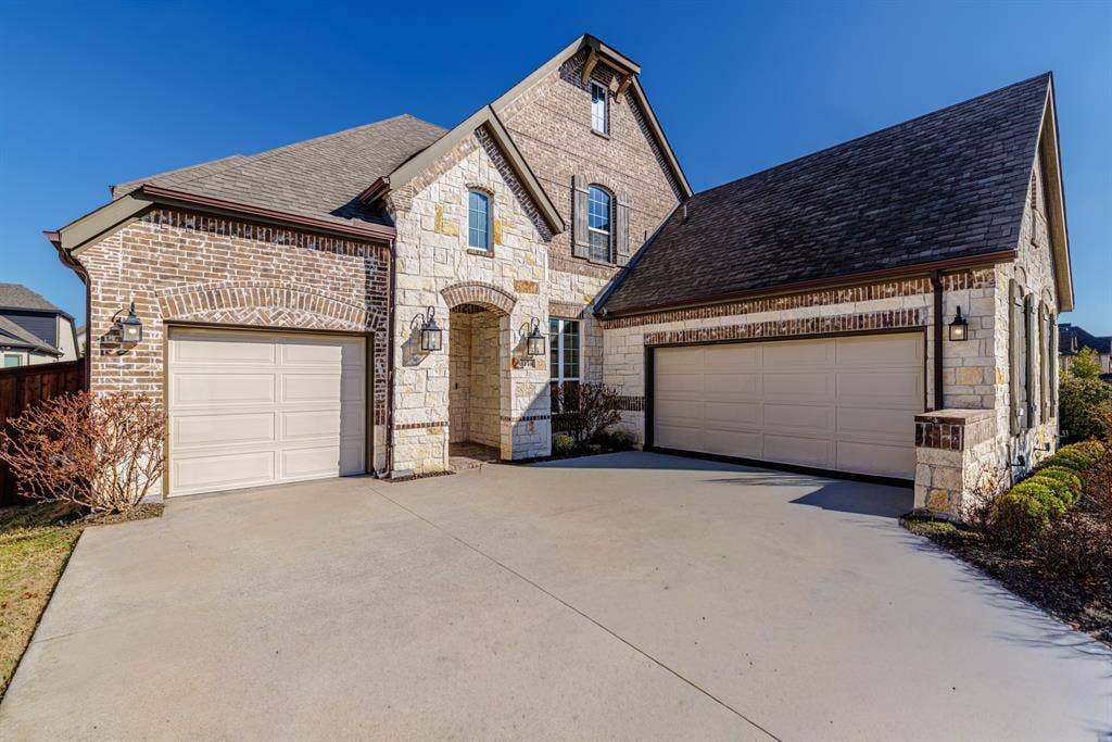 3140 Kennington Drive, Prosper, TX 75078 Stone and brick facade featuring two attached garages and a concrete driveway