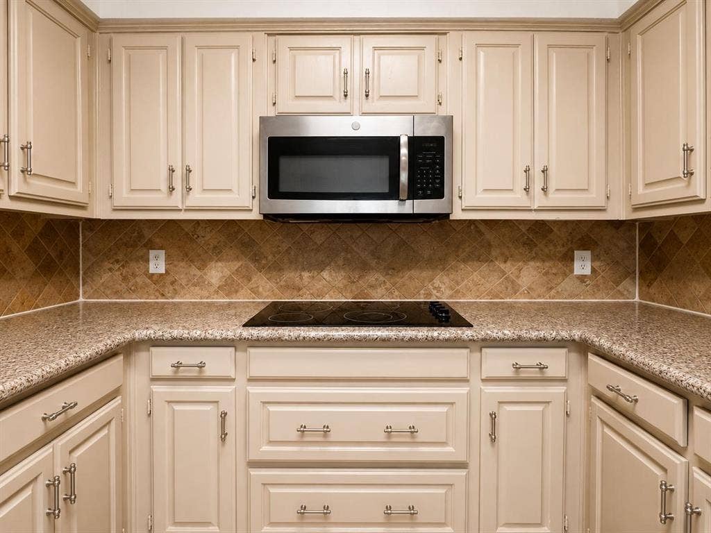 7806 Williams Avenue, Frisco, TX 75033 Kitchen featuring cream-colored cabinetry with brushed nickel hardware, a built-in stainless steel microwave, a black electric cooktop, and speckled countertops