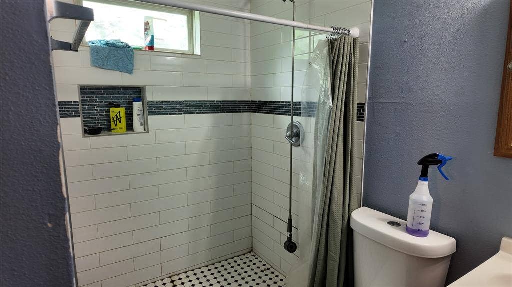 Shower enclosure featuring white subway tile, a dark accent tile band, and a hexagonal mosaic tile floor