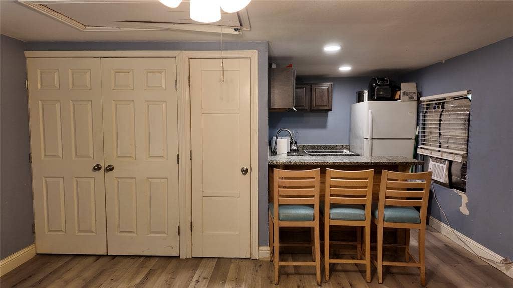 Compact kitchen area featuring wood-finish flooring, dark wood cabinetry, a built-in sink with a gooseneck faucet, a light-toned countertop, and recessed ceiling lighting