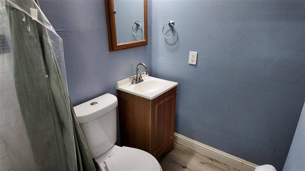 Bathroom featuring a white toilet, wood-finish vanity with an integrated sink, chrome faucet, and wood-framed medicine cabinet