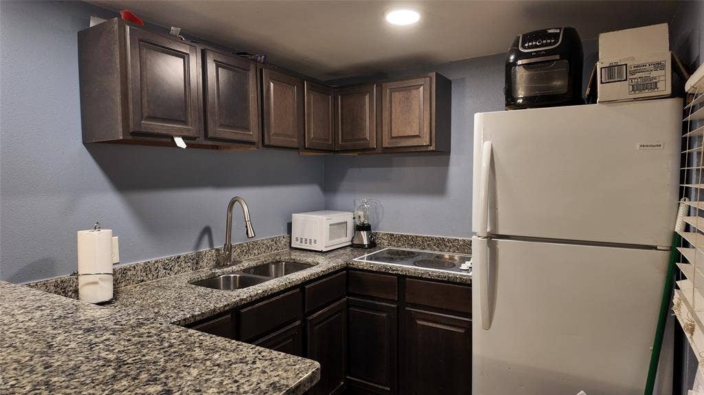 Kitchen featuring dark wood cabinetry, granite-style countertops, a double basin sink with a chrome faucet, and an electric cooktop