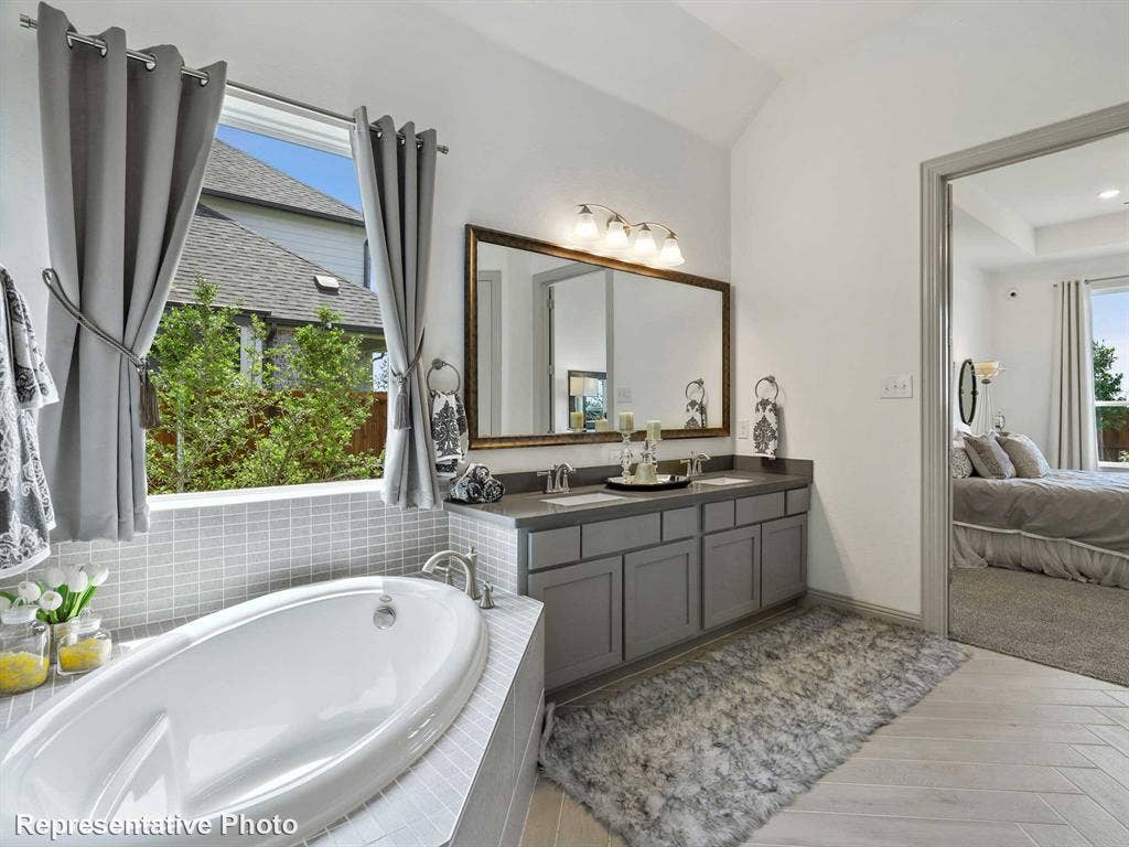 4359 Michigan Avenue, Midlothian, TX 76065 Bathroom featuring a built-in soaking tub with surrounding tile, a dual vanity with undermount sinks, a large framed mirror, and wood-finish flooring in a herringbone pattern