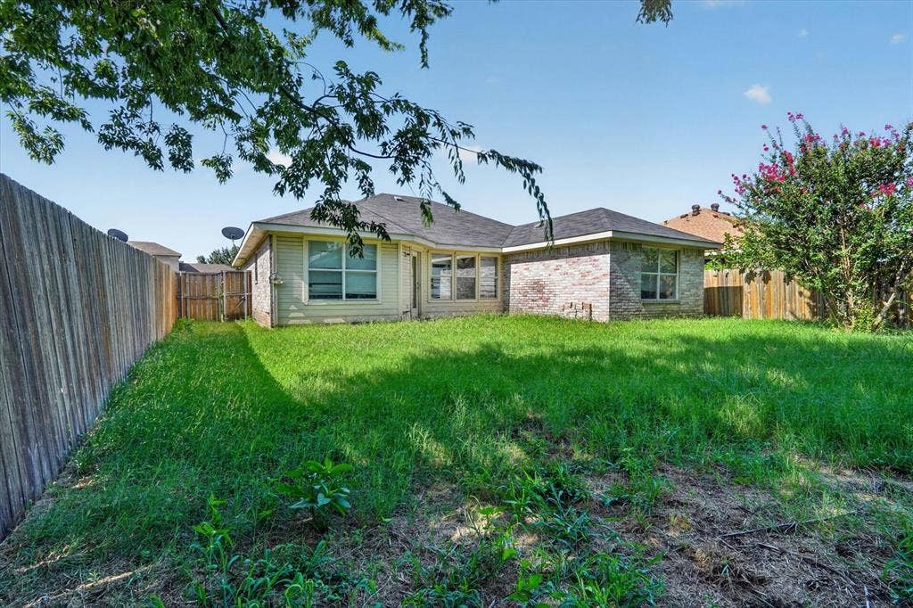 1414 Aviary Drive, DeSoto, TX 75115 Expansive backyard featuring a manicured lawn, wood fencing, and a red brick exterior