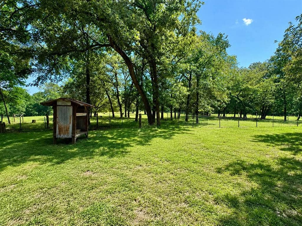7761 Fm 2494, Athens, TX 75751 Expansive green lawn surrounded by mature trees, featuring a rustic shed structure with a metal roof and weathered wood siding, and perimeter fencing