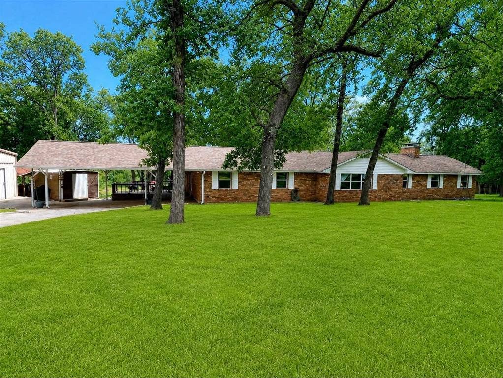 7761 Fm 2494, Athens, TX 75751 Brick exterior home featuring a covered carport, mature trees, a detached storage building, and a sprawling green lawn