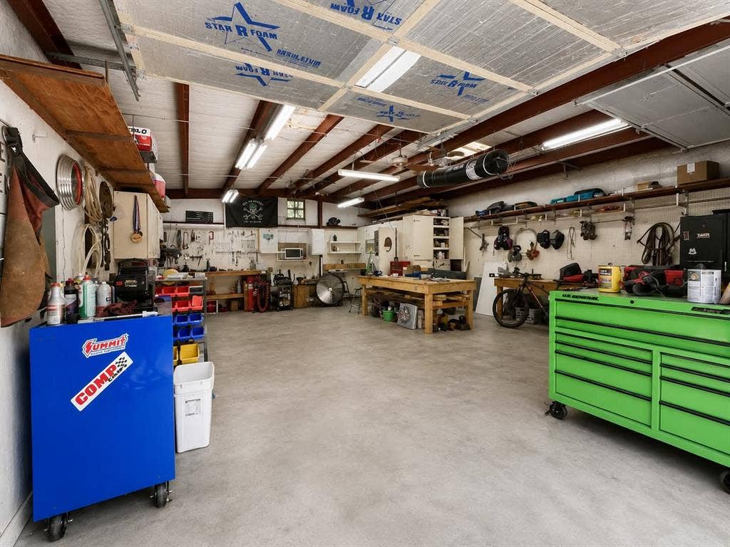 7761 Fm 2494, Athens, TX 75751 Spacious workshop area featuring a concrete floor, exposed beam ceiling with insulation panels, fluorescent lighting, extensive wall shelving, and a built-in workbench