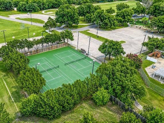 Two outdoor tennis courts with green surfacing and white line markings, surrounded by mature perimeter landscaping