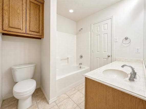 Full bathroom featuring a white tub/shower combination, light wood-finish vanity with an integrated sink, polished chrome faucet, and tiled flooring