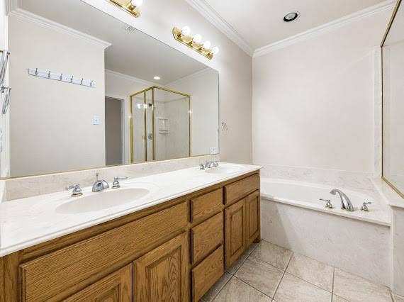 Bathroom featuring a dual vanity with wood cabinetry and light-toned countertops, an integrated soaking tub, and a separate glass-enclosed shower with gold-toned framing