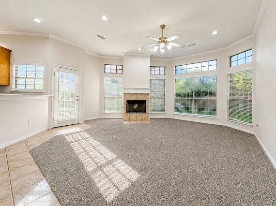 Carpeted living area featuring a tile-surround fireplace, a ceiling fan with integrated lighting, and multiple large windows with blinds