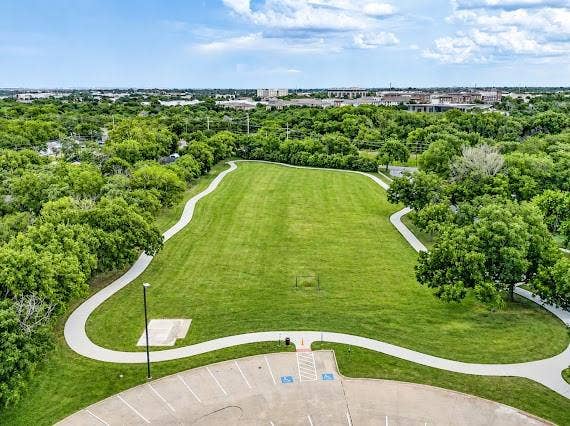 Expansive green space featuring a manicured lawn, paved walking paths, and mature trees