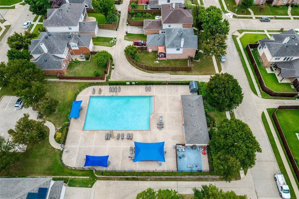 8012 Springmoss Drive, Plano, TX 75025 Community swimming pool featuring a large rectangular pool, expansive concrete deck, multiple lounge chairs, blue shade structures, and a dedicated pool house