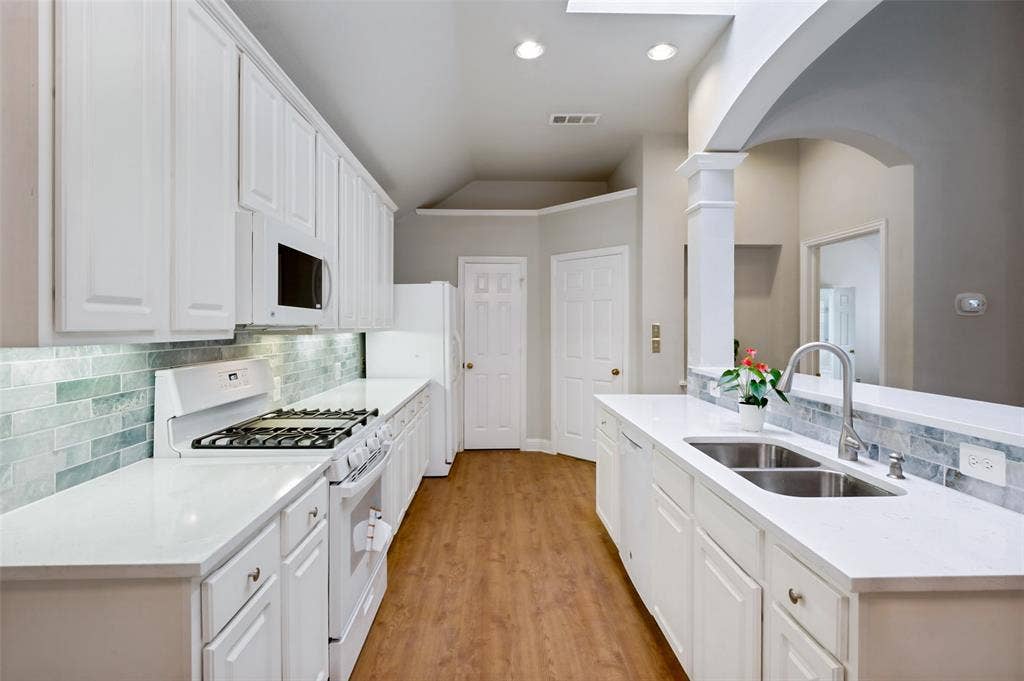 8012 Springmoss Drive, Plano, TX 75025 Bright kitchen featuring white cabinetry, gas burning stove, light counter tops, wood-finish flooring, a stainless steel double basin sink with a high-arc faucet, and an arched architectural detail