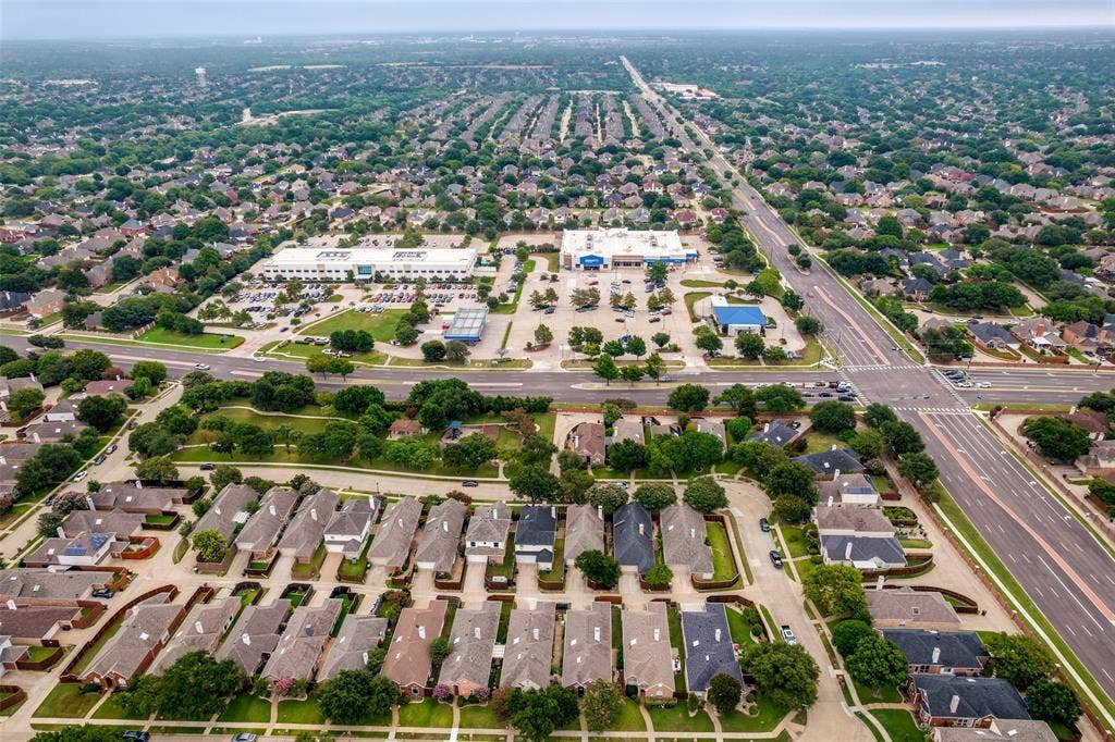 8012 Springmoss Drive, Plano, TX 75025 Expansive aerial perspective showcasing a residential neighborhood with numerous single-family homes, mature trees, and a commercial area featuring retail buildings and parking