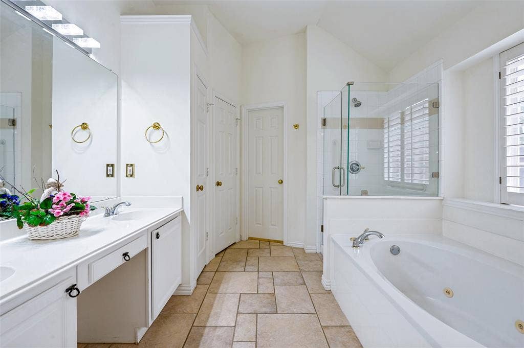 8012 Springmoss Drive, Plano, TX 75025 Spacious bathroom featuring a dual vanity, a built-in jetted tub, a glass-enclosed shower, wood shutters, and tile flooring