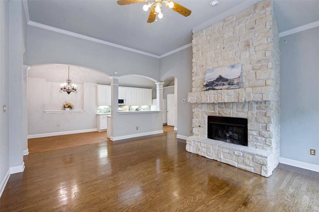 8012 Springmoss Drive, Plano, TX 75025 Stone-faced fireplace with a black hearth and mantle, wood-finish flooring, crown molding, and arched doorways