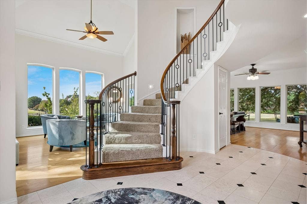 7501 Sweetgum Drive, Irving, TX 75063 Curved staircase with wrought iron balusters and wood handrail, vaulted ceiling, arched windows, and tile flooring with accent squares