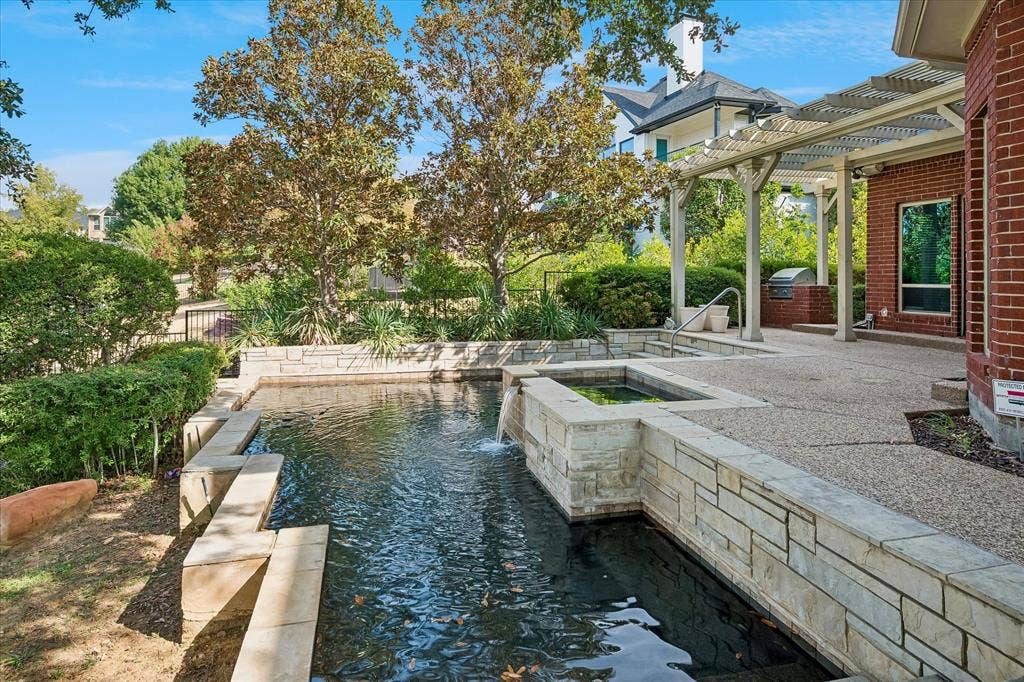 7501 Sweetgum Drive, Irving, TX 75063 Outdoor stone water feature with integrated spa, adjacent to a textured concrete patio and attached pergola
