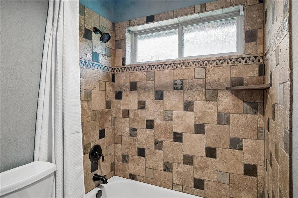 7501 Sweetgum Drive, Irving, TX 75063 Tiled shower surround with decorative mosaic accent, built-in shelving, and frosted window