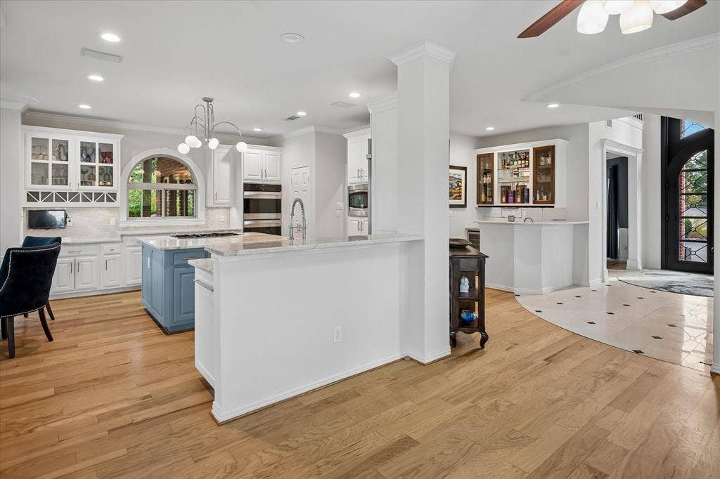 7501 Sweetgum Drive, Irving, TX 75063 Kitchen featuring a blue island, white cabinetry, integrated double ovens, and a large arched window