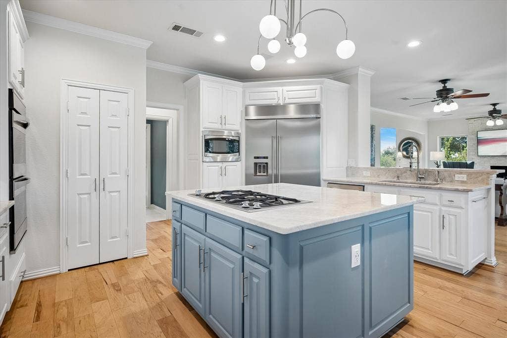 7501 Sweetgum Drive, Irving, TX 75063 Kitchen featuring wood-finish flooring, a central island with a built-in cooktop, white perimeter cabinetry, stainless steel appliances, and stone countertops